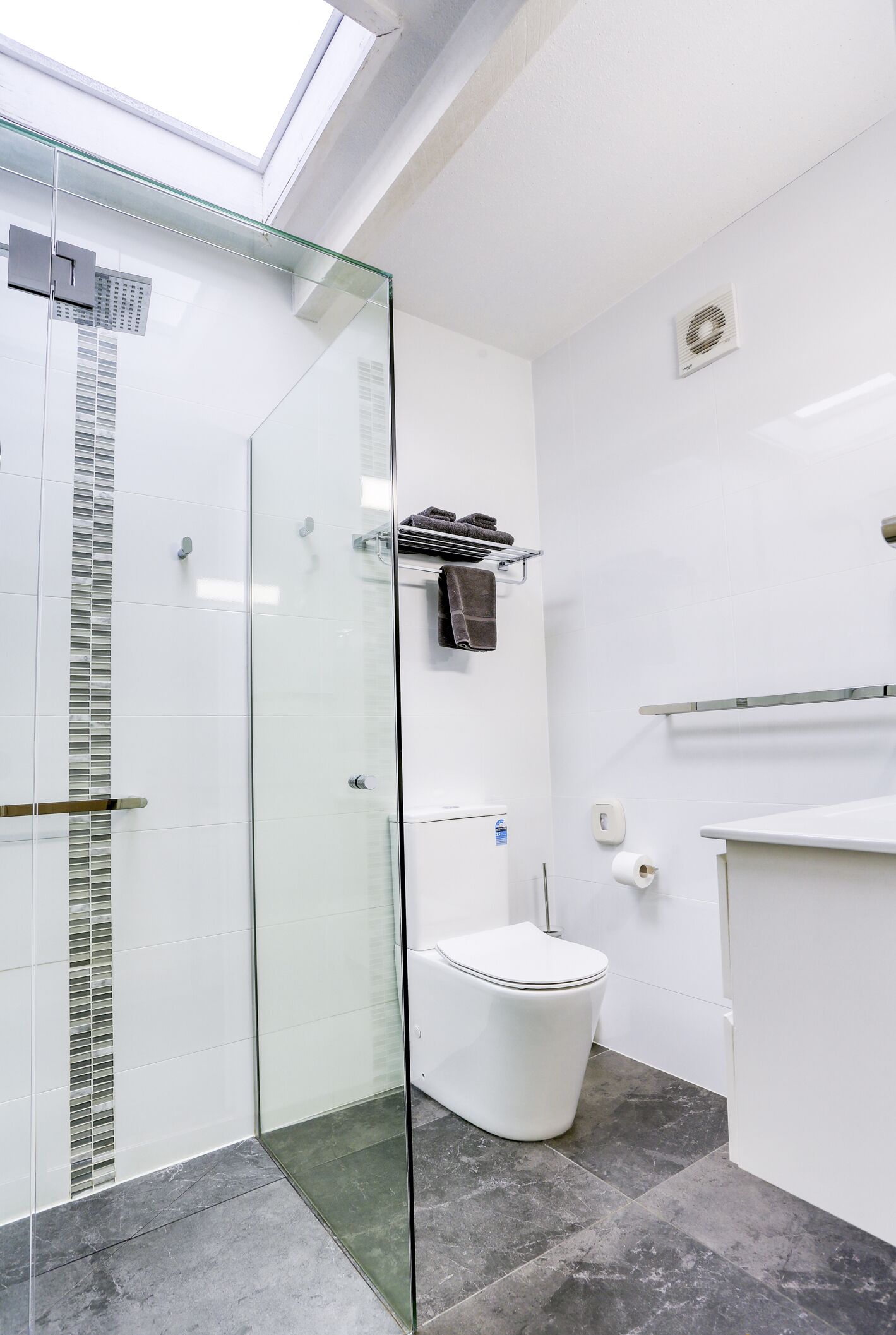 Une salle de bain moderne avec une douche à l’italienne en verre, des carreaux blancs et une lucarne bien visible.