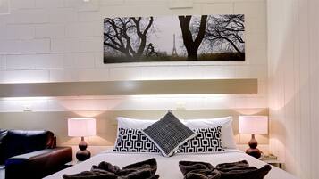 Habitación de hotel con cama, dos almohadas, manta, mesita de noche, lámpara, teléfono y un cuadro colgado en la pared.