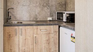Una cocina compacta con microondas integrado, un lavamanos y armarios de madera.