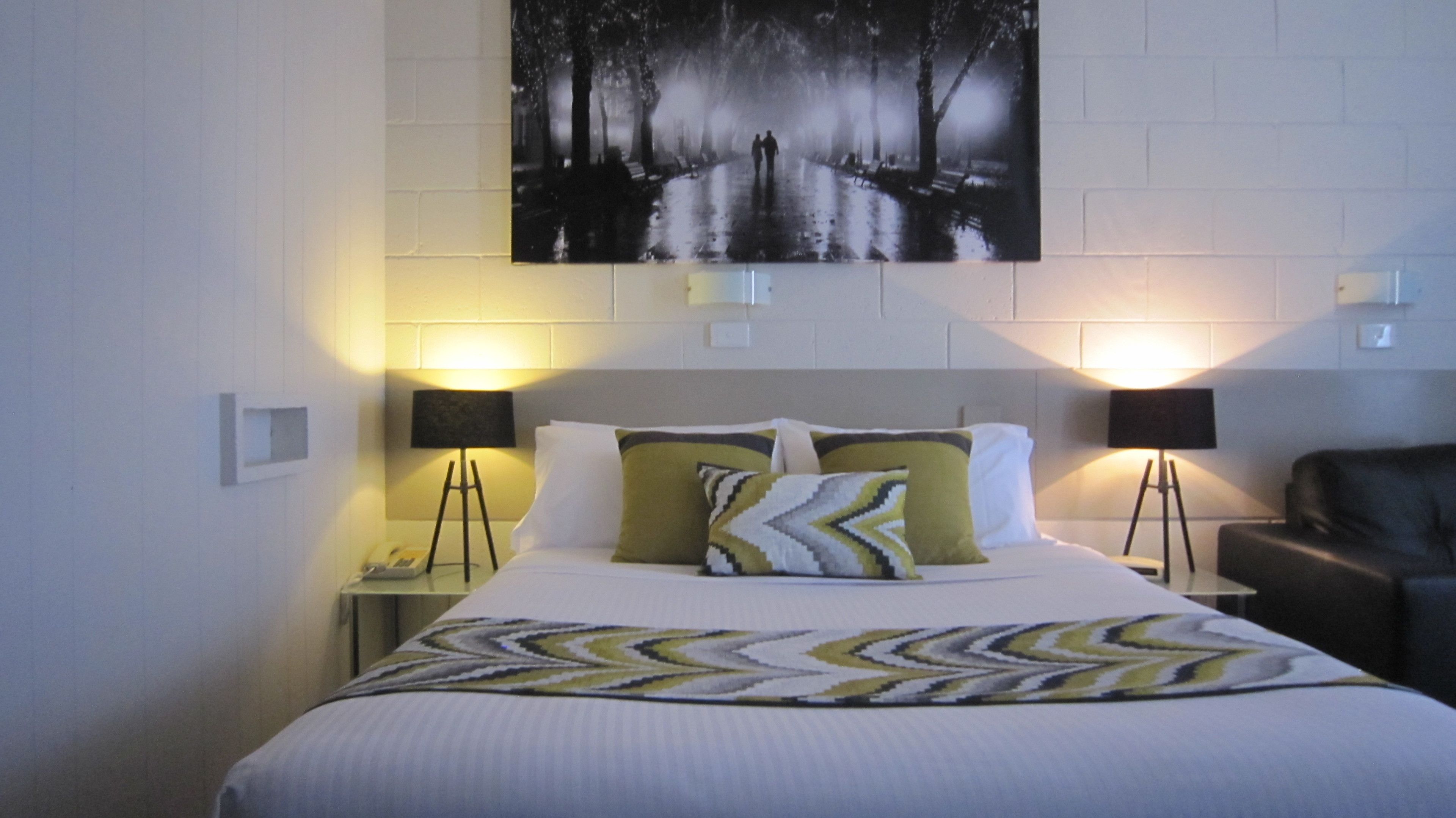 A hotel room with a bed, two bedside lamps, a nightstand, and a painting on the wall.