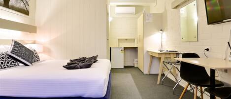 A hotel room with a bed, a desk, a chair, a mirror, and a small kitchenette.