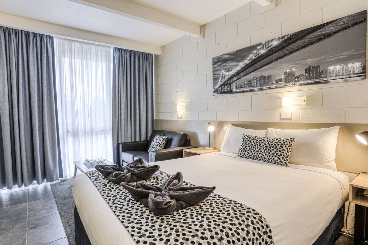 A hotel room with a large bed, a cityscape artwork on the wall, a city view through the window, and a modern design.