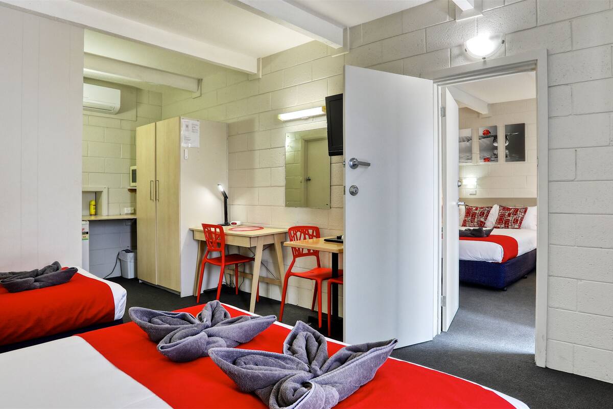 A hotel room with a bed, a desk, two chairs, a mirror, and a door leading to another room.