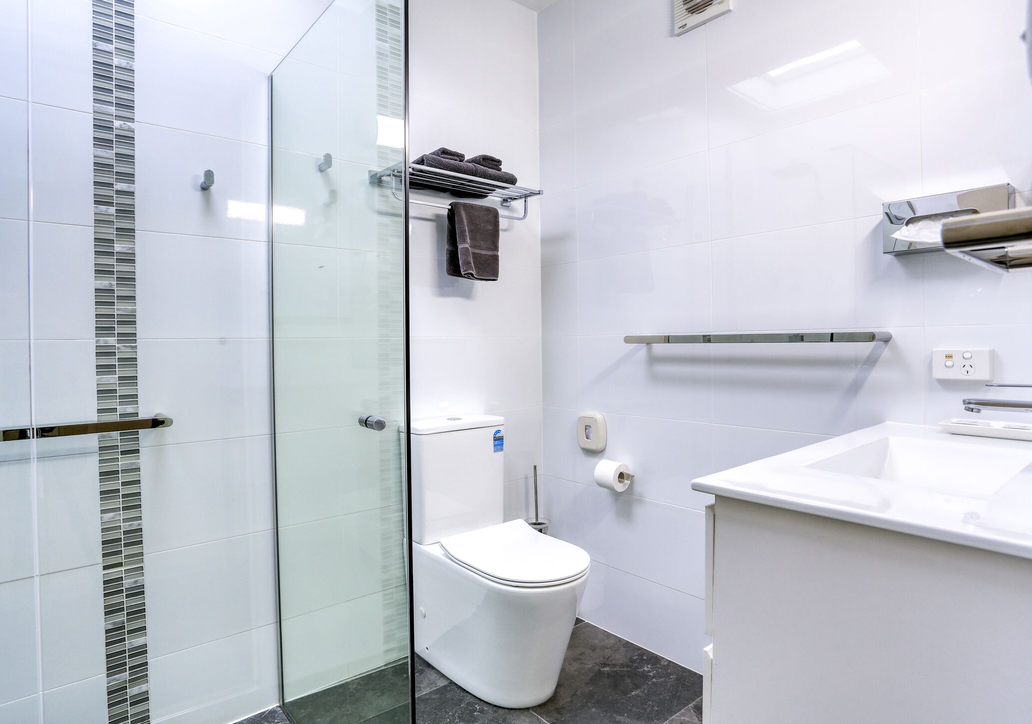 A modern bathroom with a glass shower enclosure, a white toilet, a sink with a mirror, and a towel rack.