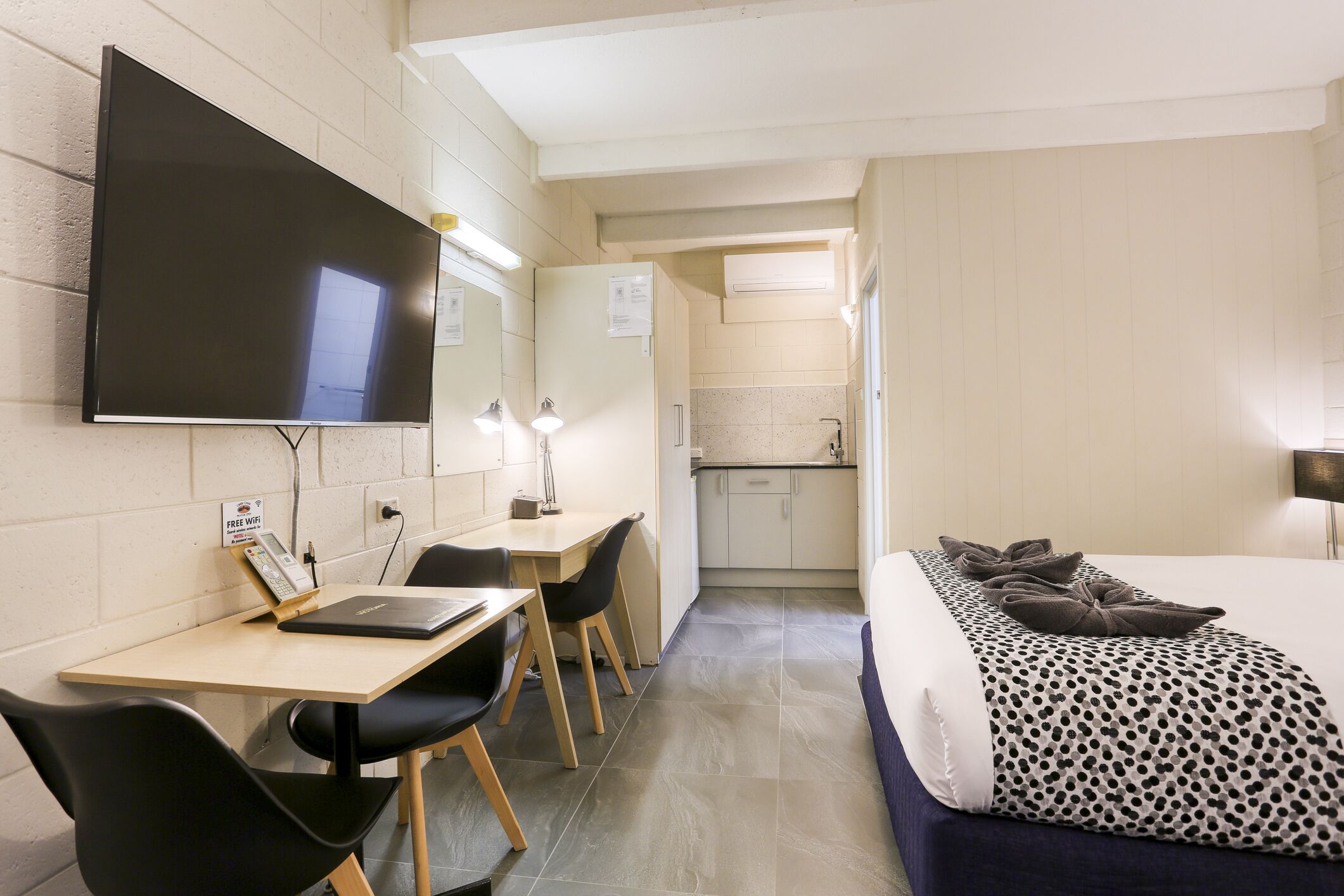 Una habitación de hotel con cama, escritorio, laptop, televisión y kitchenette.