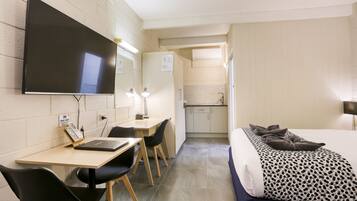 Una habitación de hotel con cama, escritorio, laptop, televisión y kitchenette.