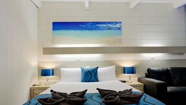Habitación de hotel con una cama grande, dos lámparas de noche, un cuadro de una playa y un sillón de cuero negro.