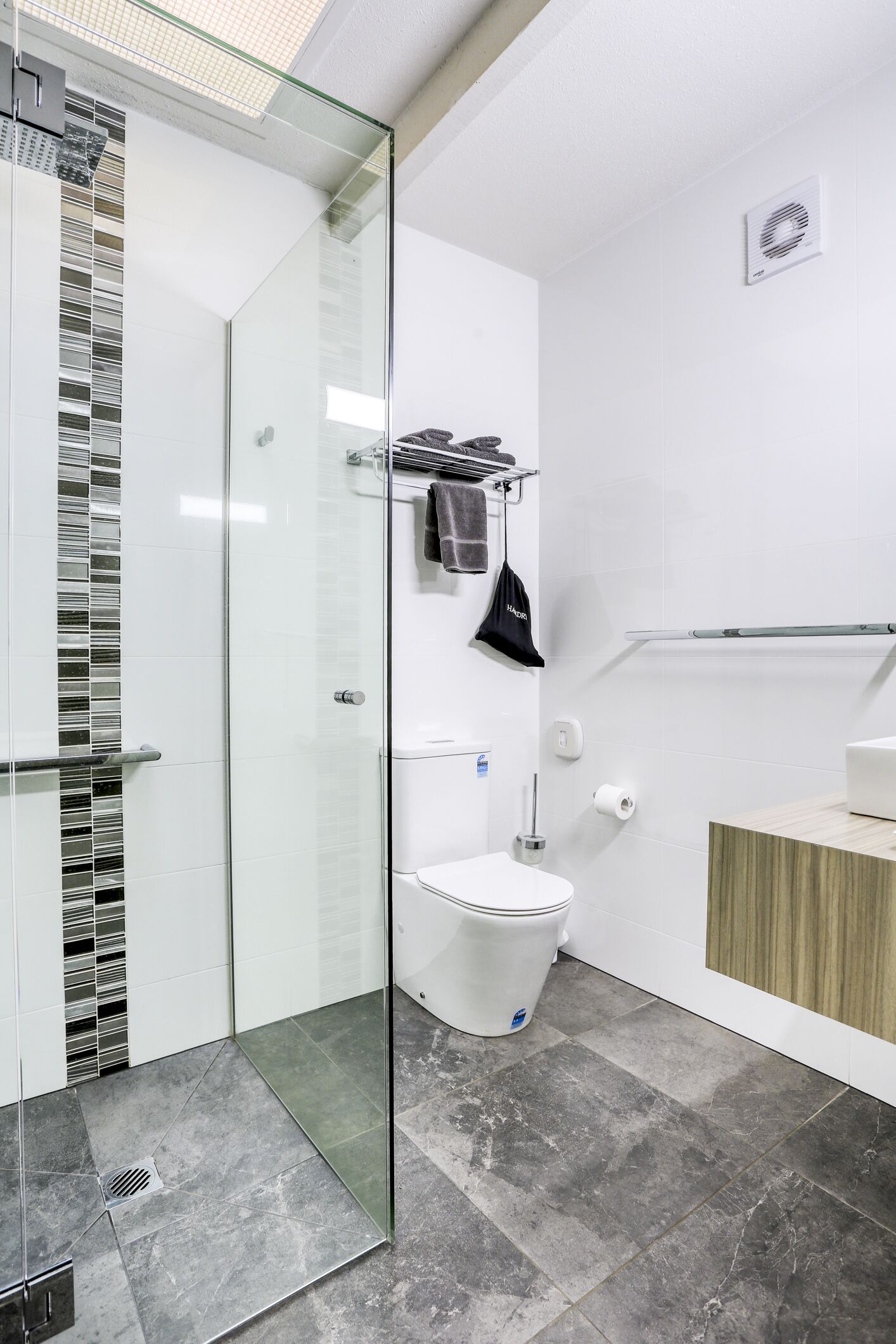 A modern bathroom with a glass shower enclosure, a toilet, and a vanity with a towel rack.