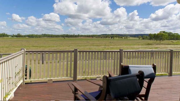 A wooden deck with two chairs and a view of a grassy field under a partly cloudy sky. - Lee Farm Stay Cottages (Booie)
