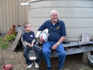 A man and a child sitting on a bench outdoors, holding a basket of eggs. - Lee Farm Stay Cottages (Booie)