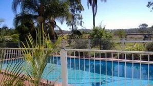 A swimming pool with a metal fence, surrounded by palm trees and other greenery. - Lee Farm Stay Cottages (Booie)