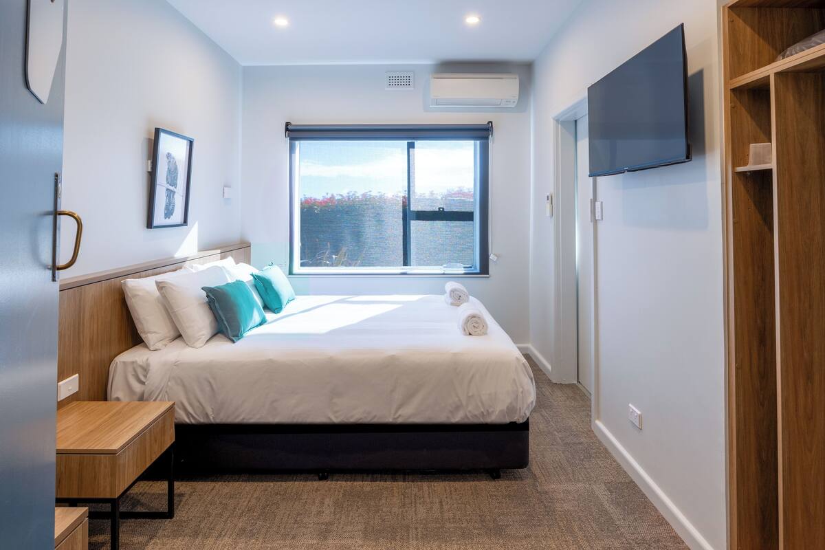 Moderni hotellihuone, jossa on suuri sänky, työpöytä, televisio ja ikkuna, josta avautuu näkymä vesistöön.