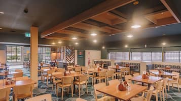 A spacious restaurant with multiple tables and chairs, a patterned floor, and a high ceiling with wooden beams.