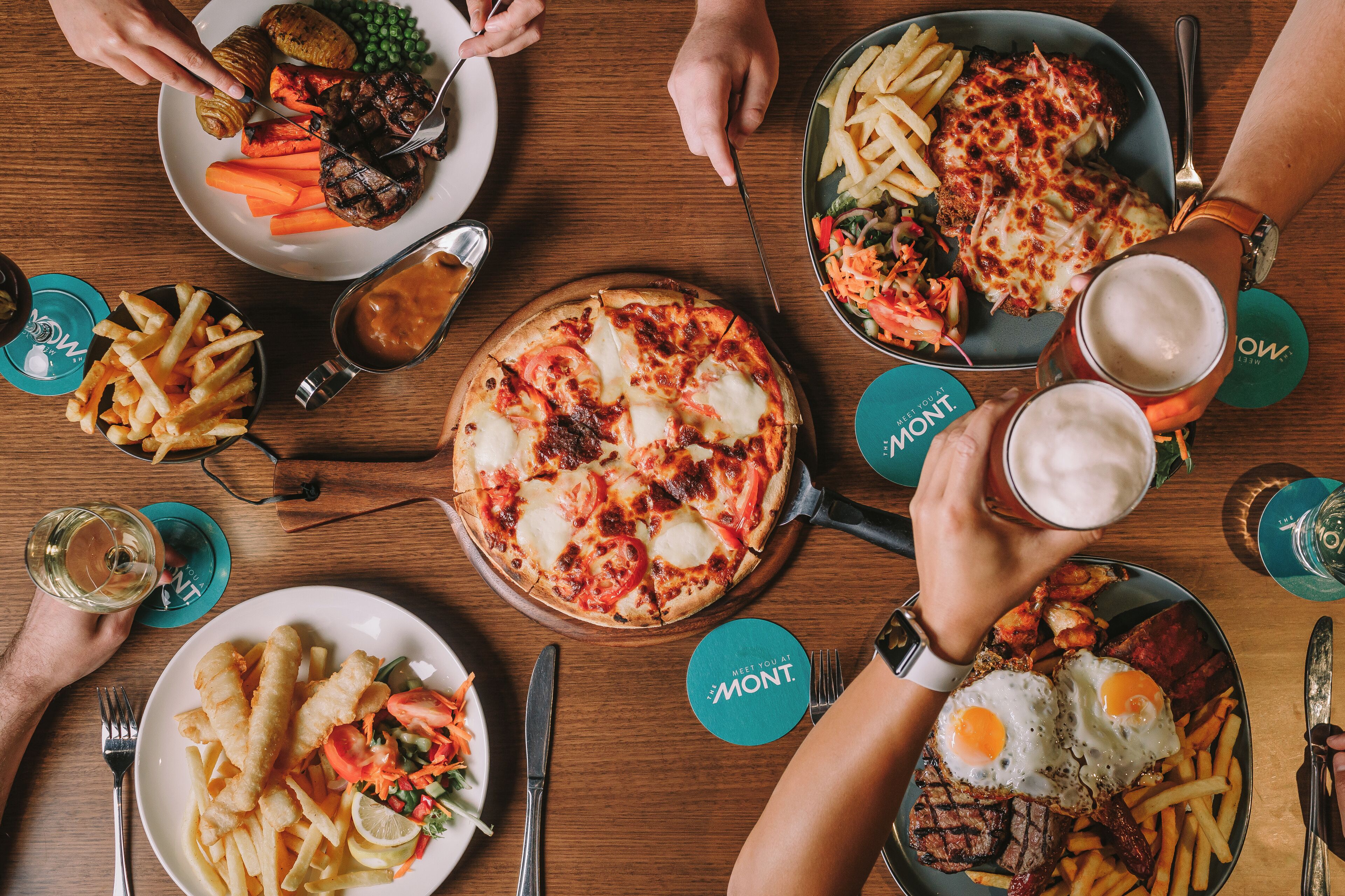 A dining table with various dishes, including pizza, fries, and meat, along with drinks and utensils.