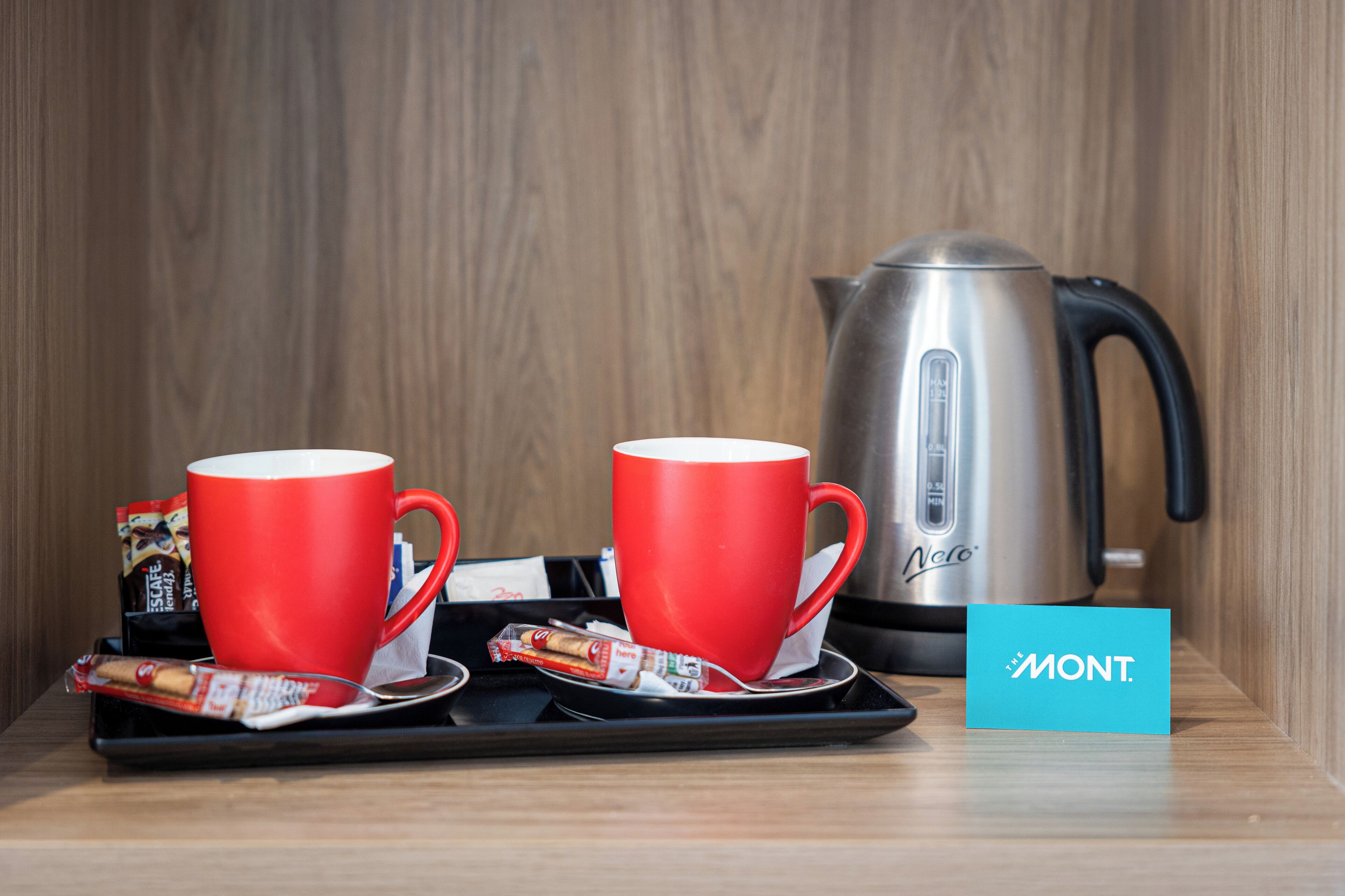 Una bandeja con dos tazas rojas y una tetera plateada sobre una superficie de madera.