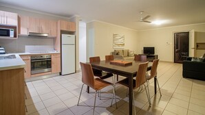 A modern kitchen with a dining area, including a table and chairs, a refrigerator, oven, and microwave. - Coochiemudlo Island Seminara Apartments (Coochiemudlo Island)