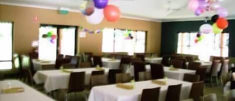 A banquet hall with tables set for dining, balloons hanging from the ceiling, and a ceiling fan.