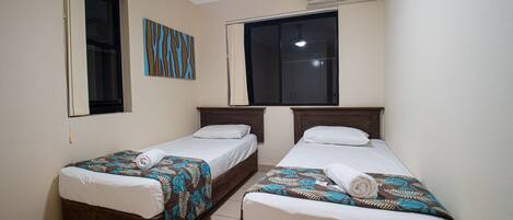 A room with two single beds, a ceiling fan, an air conditioning unit, and a window with curtains.