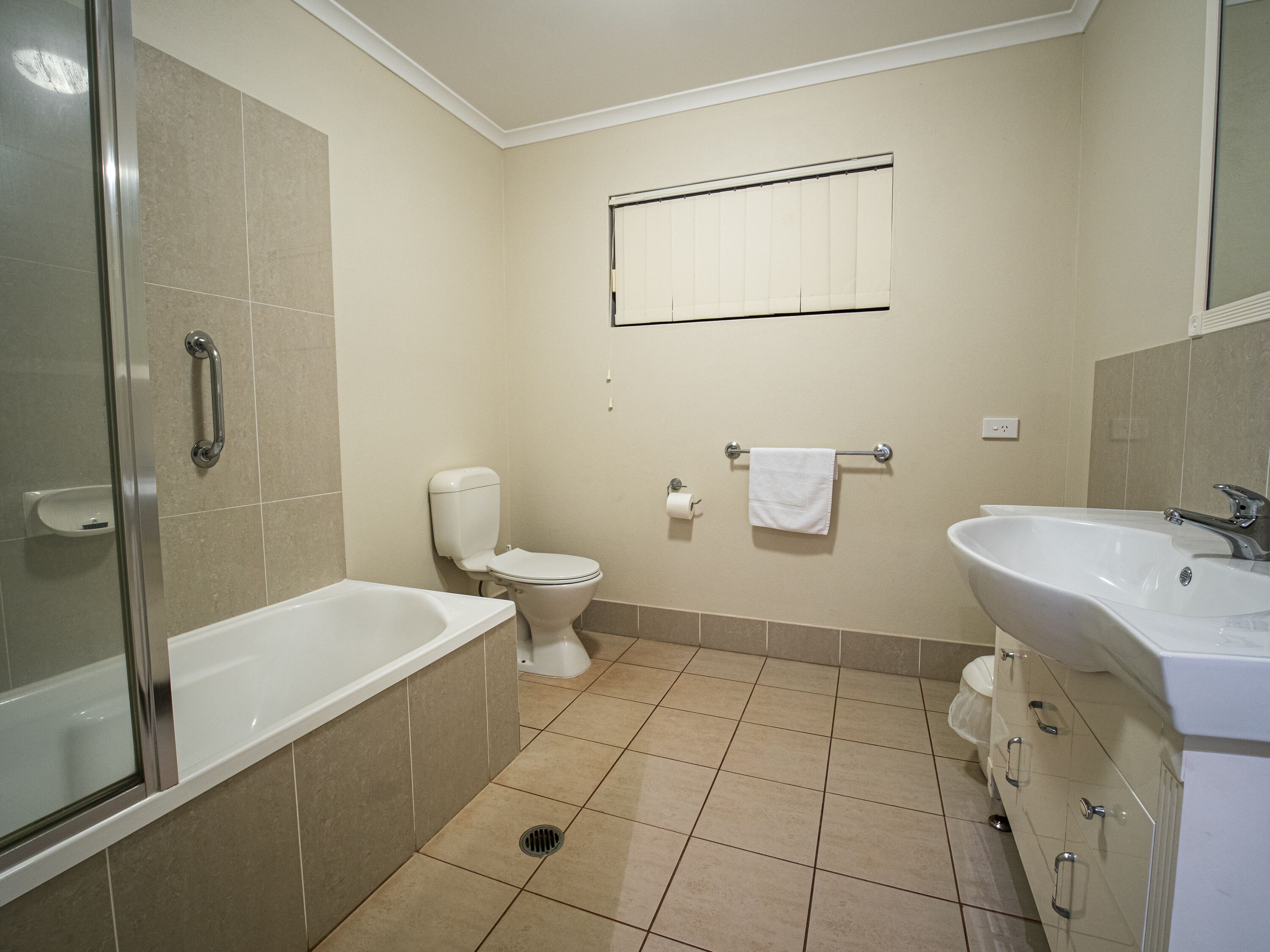 A bathroom with a shower, toilet, sink, and a towel rack.