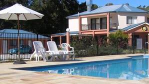 A pool area with lounge chairs and umbrellas, a building with a balcony, and a fenced garden. - Coochiemudlo Island Seminara Apartments (Coochiemudlo Island)