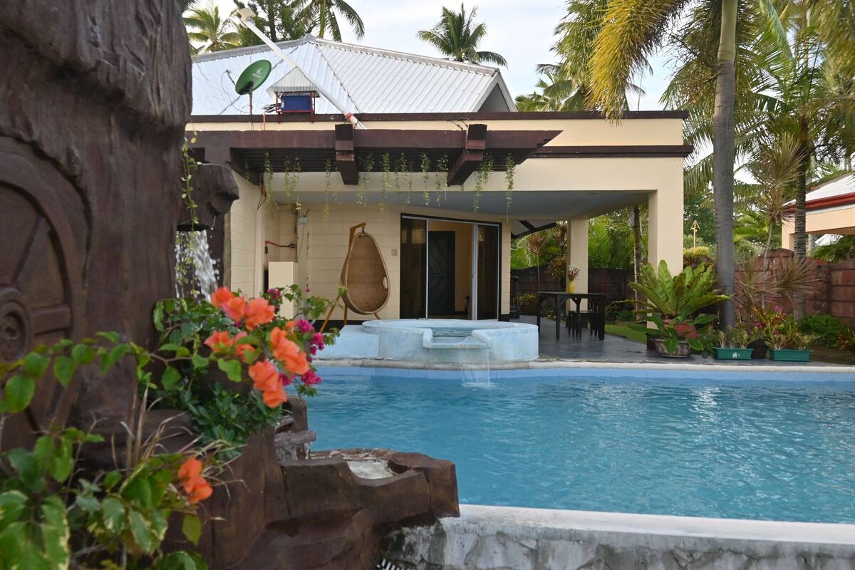 A pool area with a stone wall, a hot tub, and a covered seating area with a chair and table.