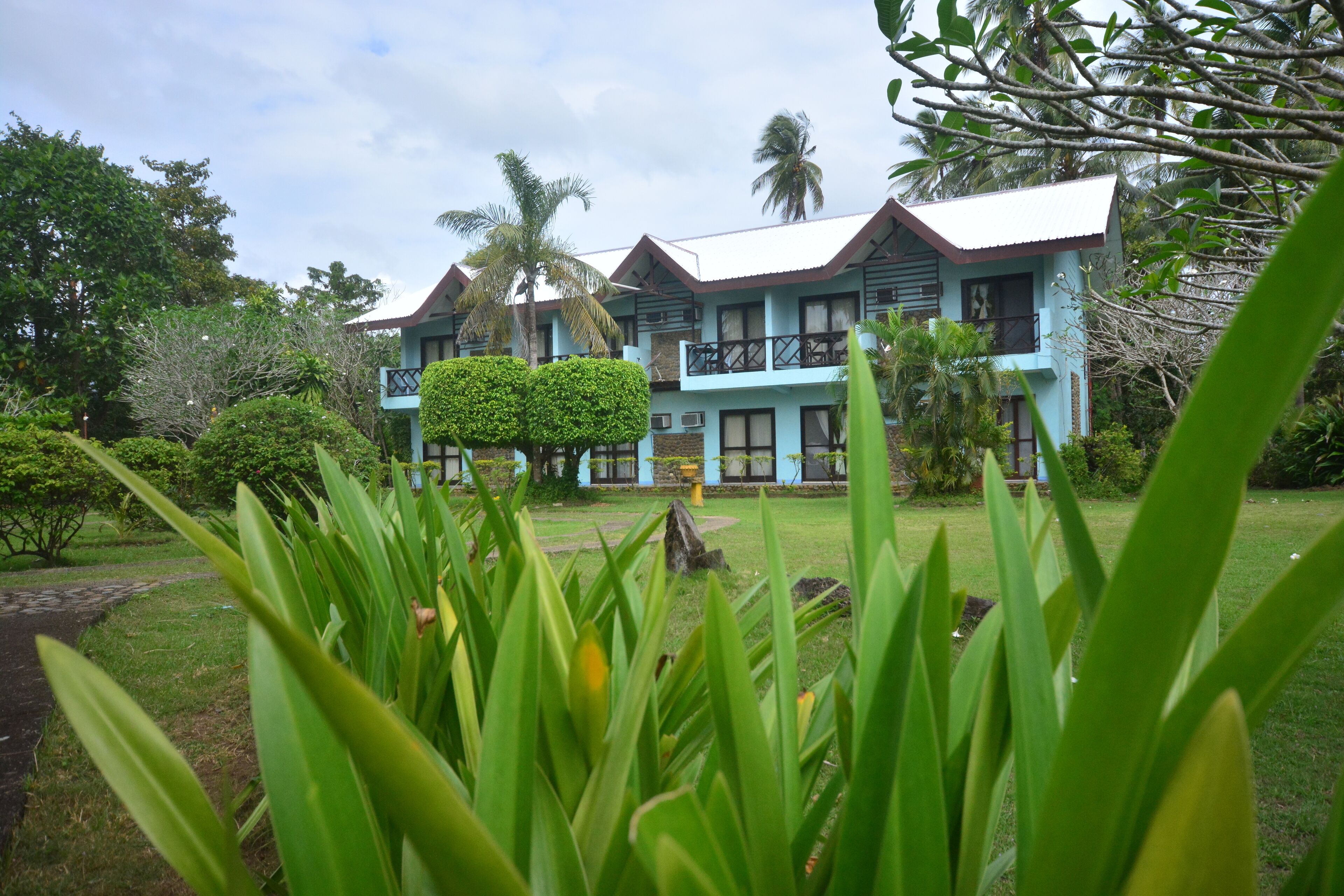 A hotel with multiple two-story buildings, a well-maintained garden with various plants, and a clear sky.