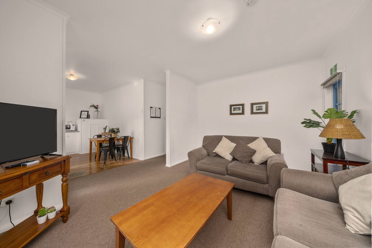 A living room with a TV, sofa, coffee table, and a dining area with chairs and a table.