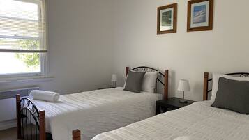 A bedroom with two single beds, a window with blinds, a radiator, and two framed pictures on the wall.