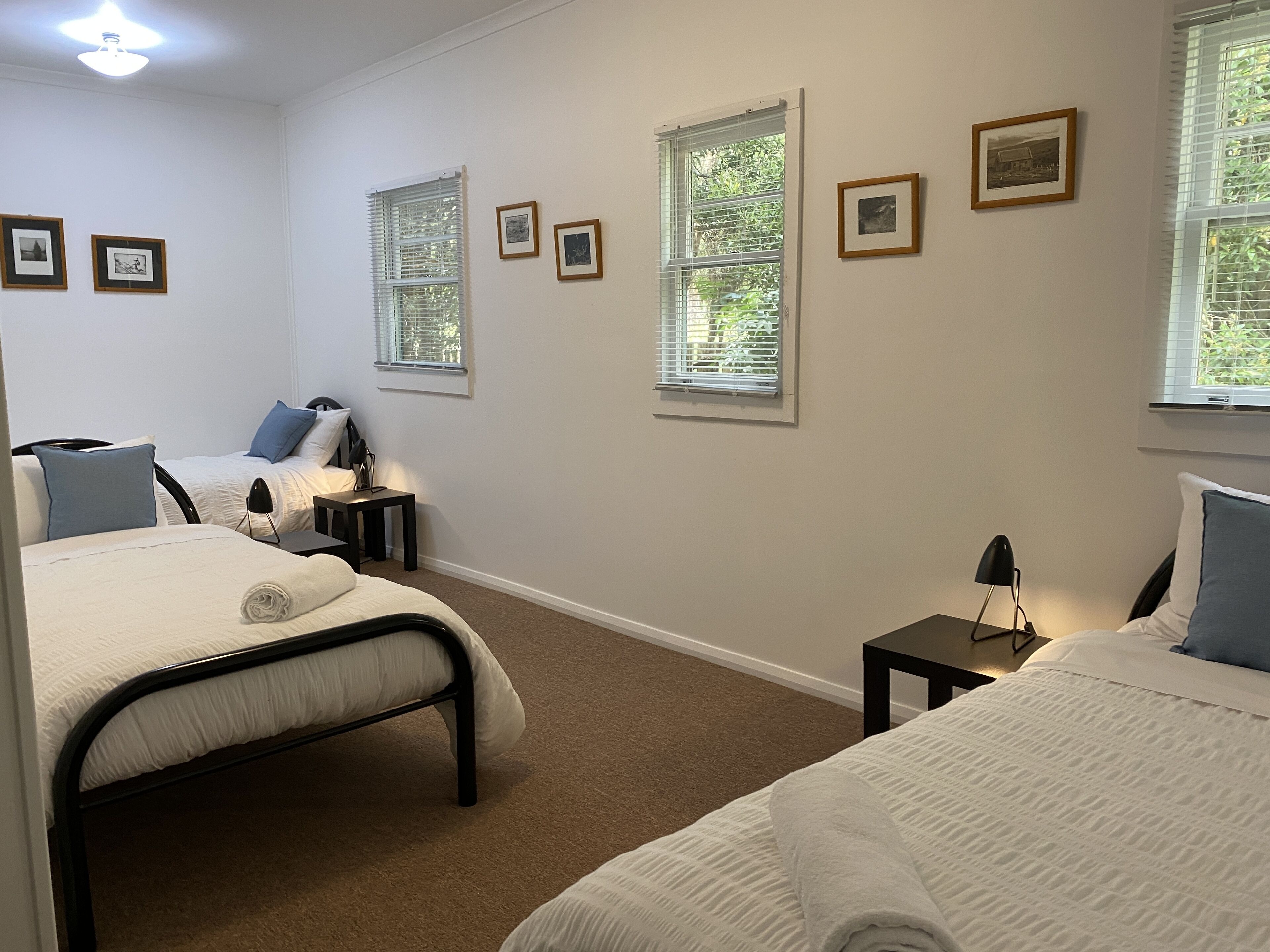 A hotel room with two beds, a small table, a chair, and a window with blinds.