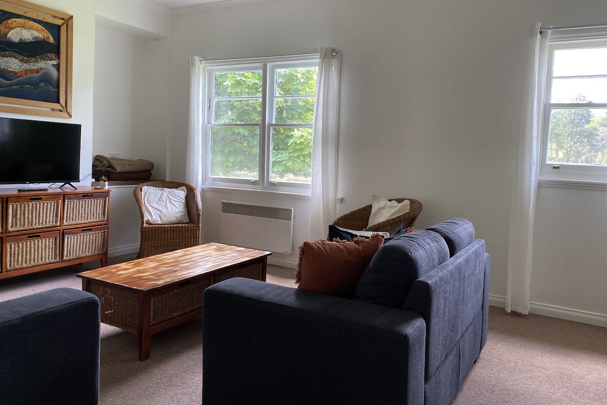 A living room with a television, wicker furniture, a sofa, and a window with a view of greenery.