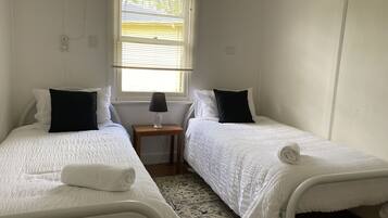 A twin room with two beds, a small table with a lamp, and a window with blinds.