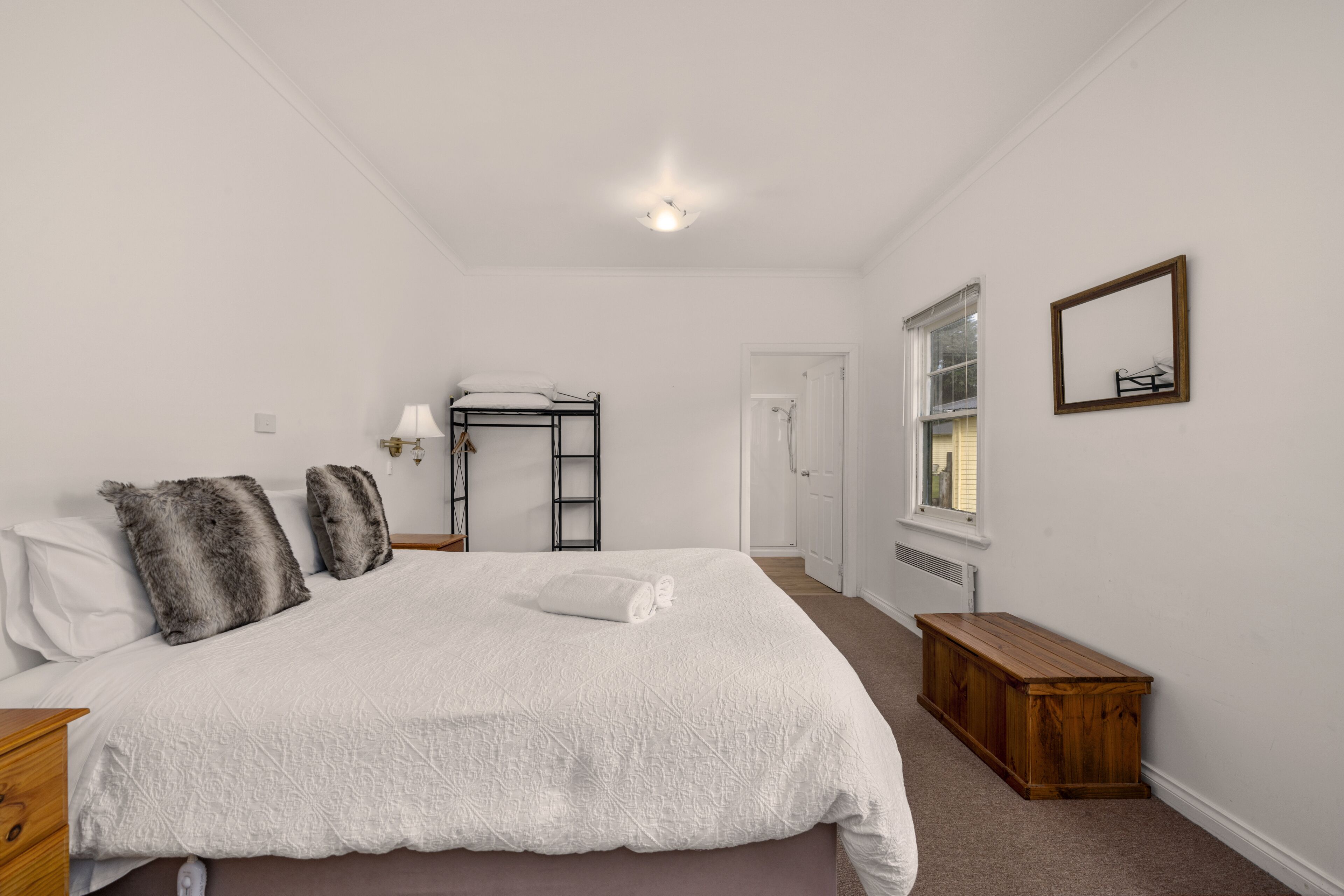 Een slaapkamer met een groot bed, een houten bankje, een ladder en een raam.