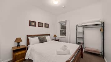 Een keurig opgemaakt slaapkamer met een bed, nachtkastje, lamp en een stapelbed.