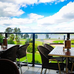 Restaurante com mesas ao ar livre, vista para a água e para uma estrada.