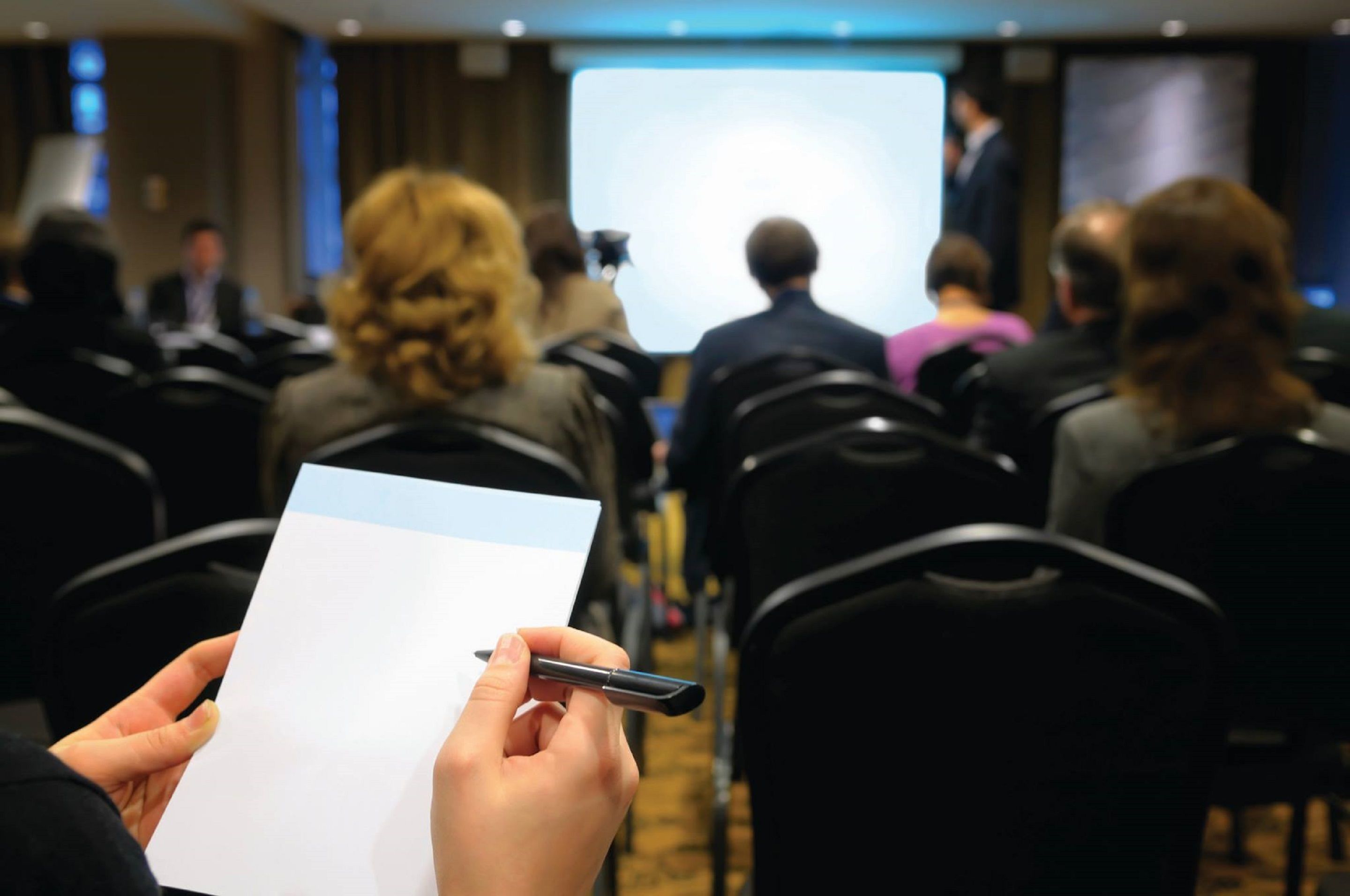 Sala de conferências com fileiras de cadeiras voltadas para uma tela de projeção.