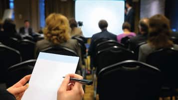 Sala de conferências com fileiras de cadeiras voltadas para uma tela de projeção.