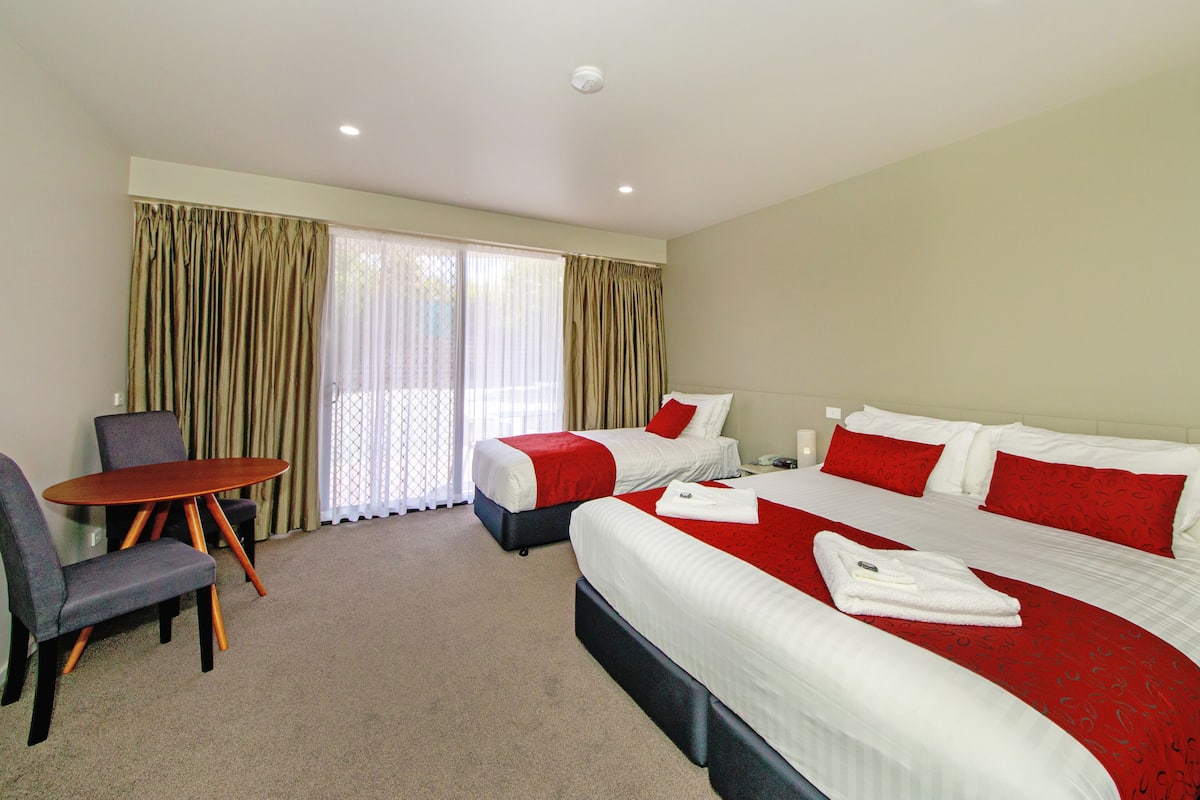 A hotel room with two beds, a small table, and a chair.