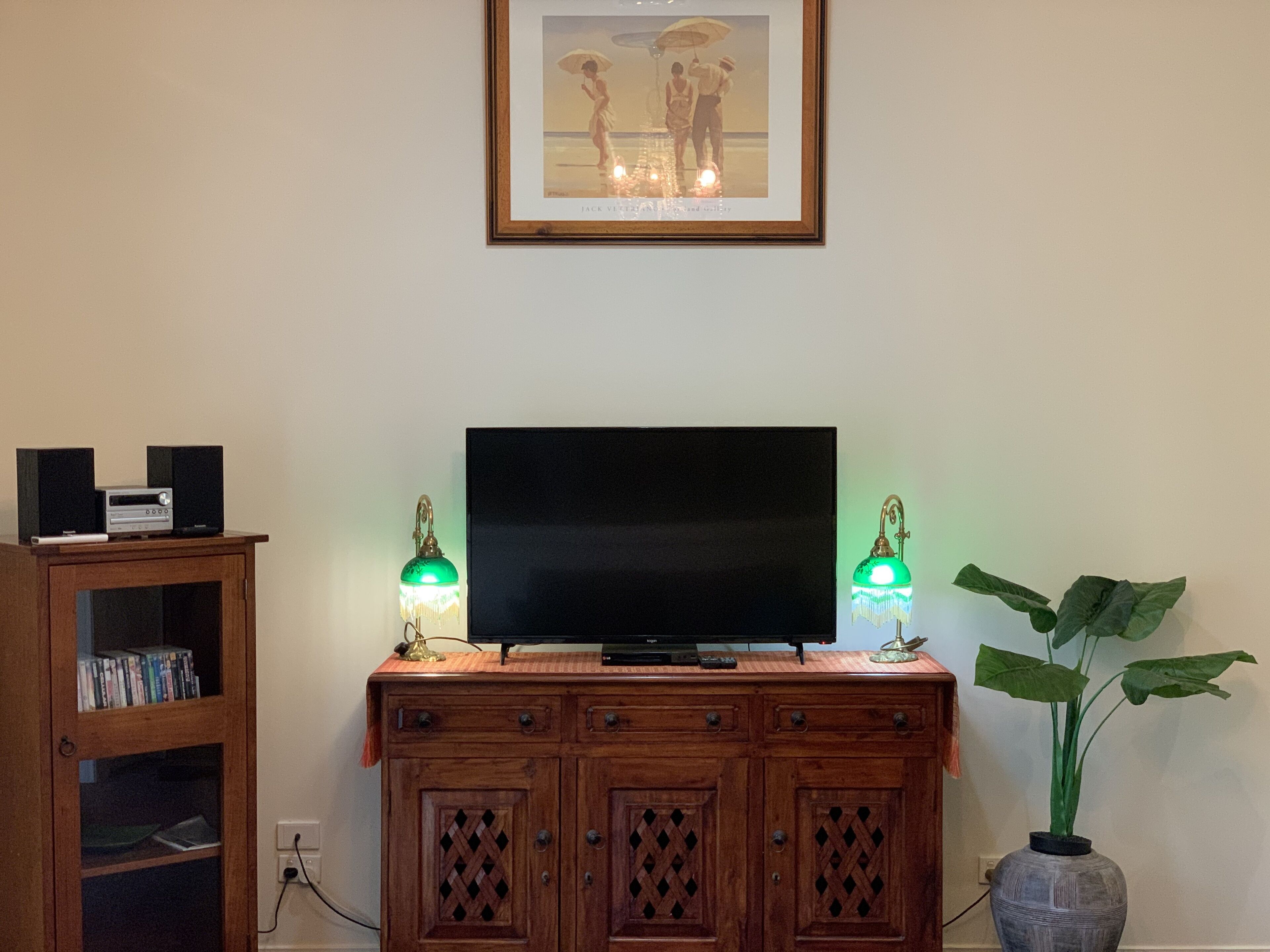 Un mueble de madera con un televisor de pantalla plana, dos lámparas de mesa verdes y un cuadro enmarcado encima.