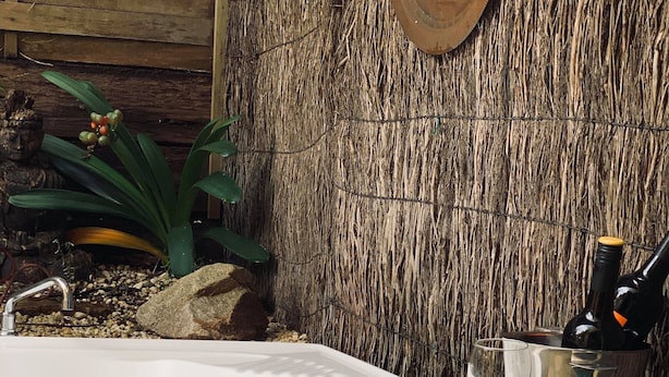 Een hottub met een rustieke houten achtergrond, een metalen emmer met glazen, en een rozenstruik op de voorgrond.