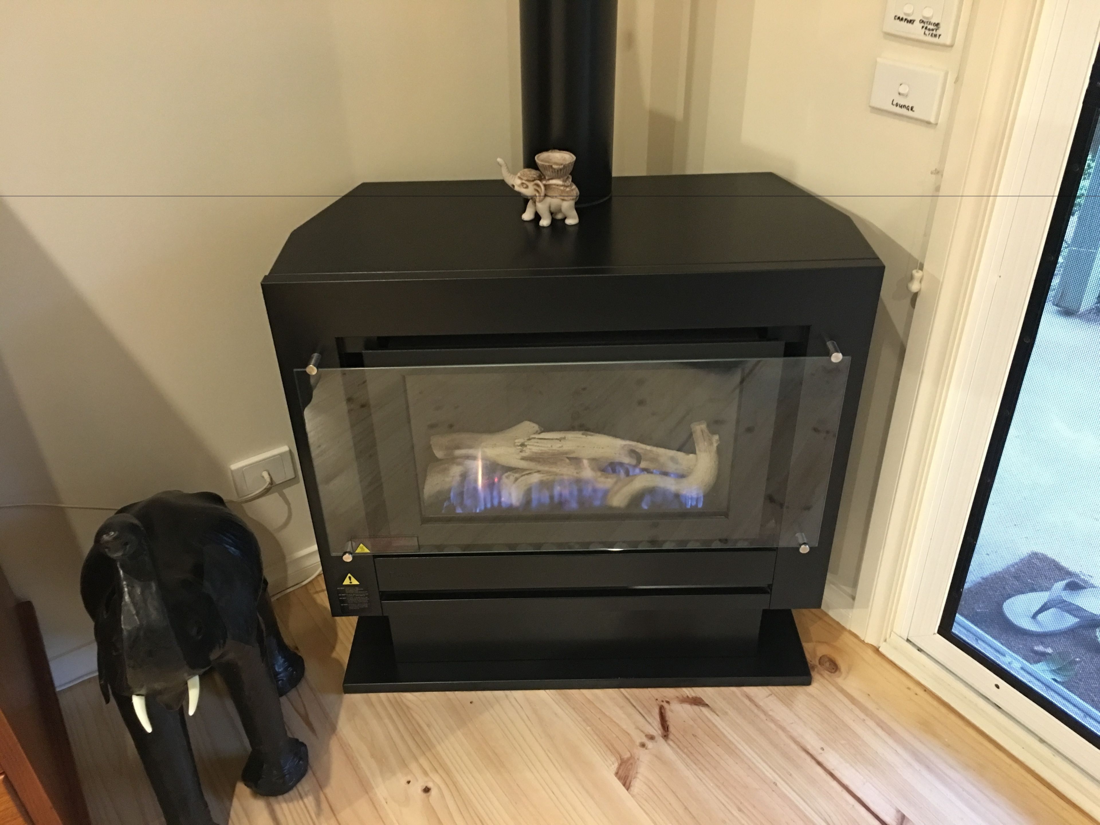 A black wood-burning stove with a glass front, a small figurine on top, and a dog statue beside it.