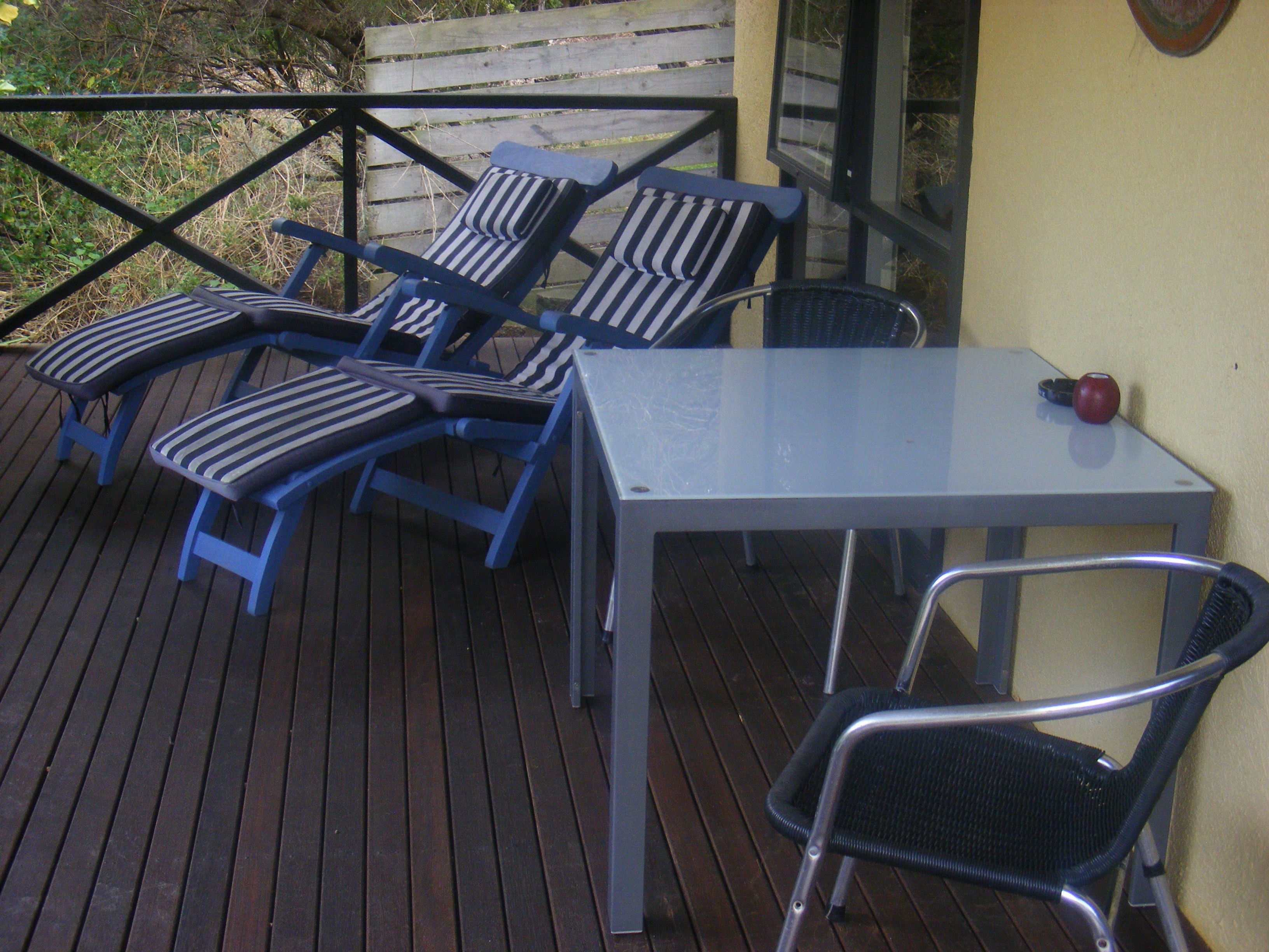 A deck with two lounge chairs and a table, a small chair, and a red apple on the table.