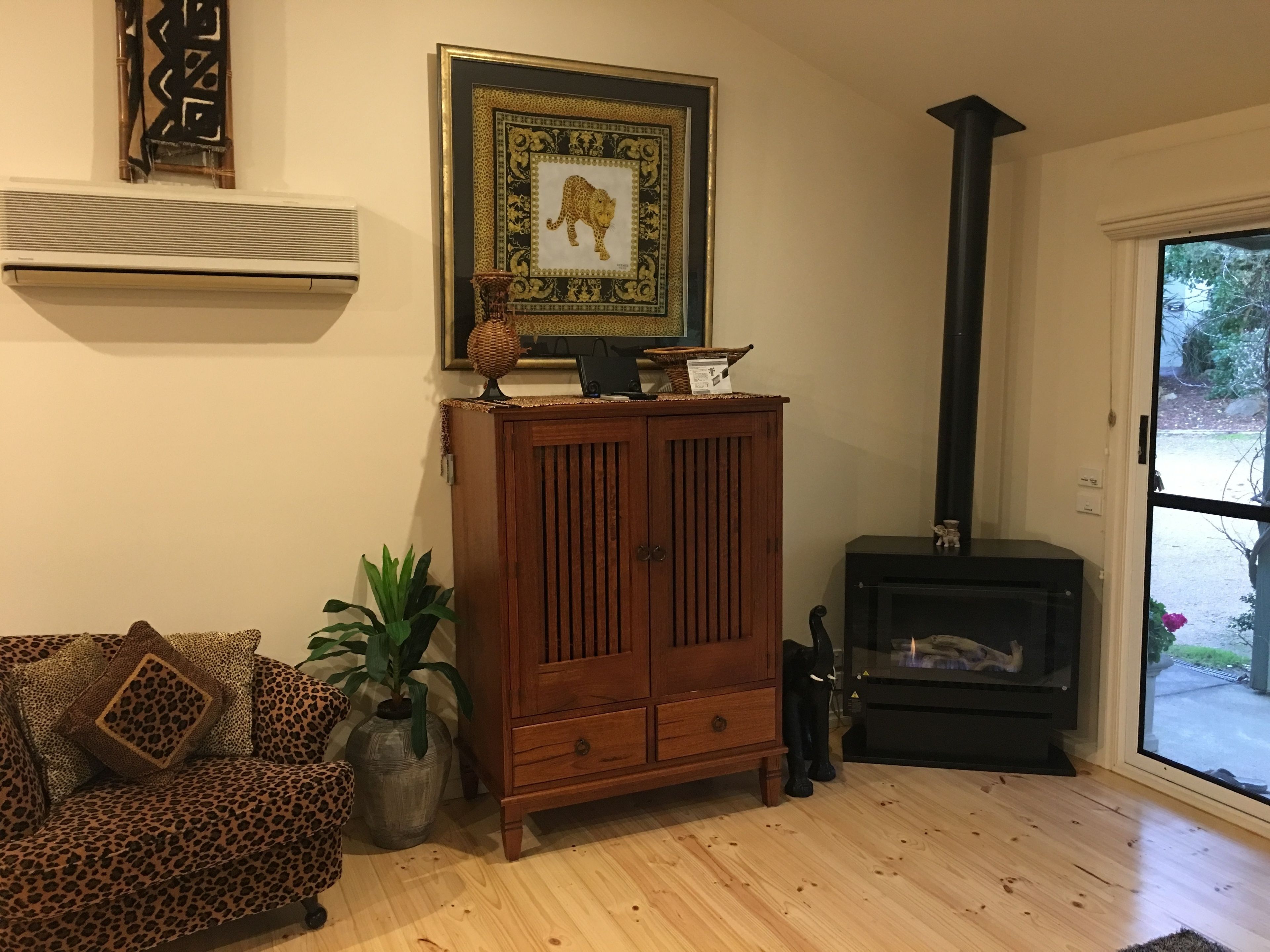 Uma sala de estar com um armário de madeira, um sofá estampado com onça, uma planta em vaso, um quadro emoldurado e uma lareira preta.