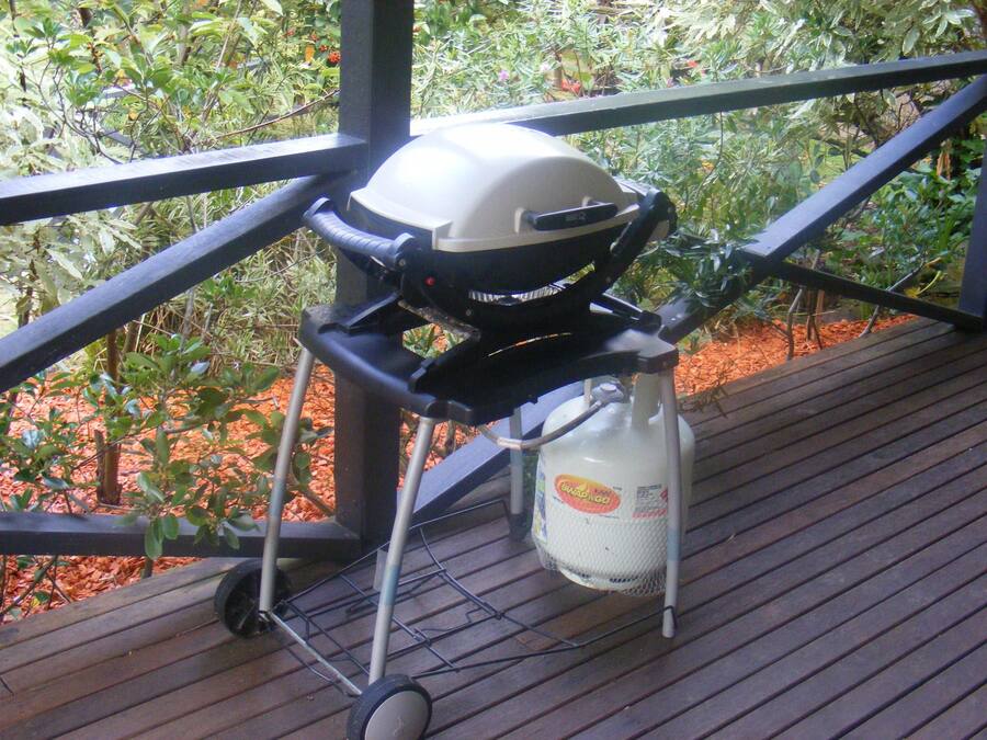 A barbecue grill on a wooden deck with a metal railing, surrounded by greenery.