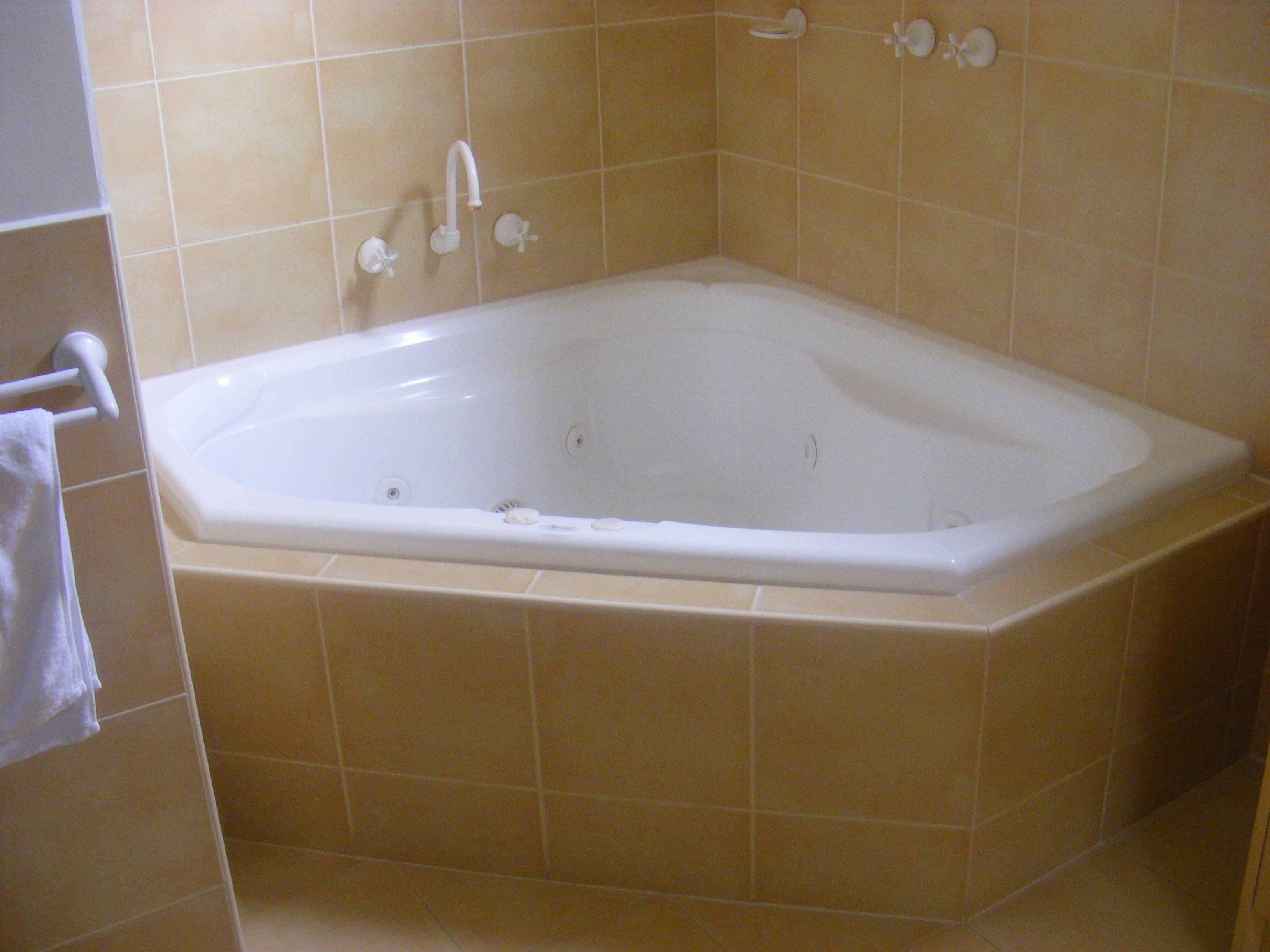 A standard rectangular bathtub with a single faucet and a handheld showerhead, set against beige tiled walls.