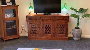 A wooden entertainment center with a flat-screen TV, two green desk lamps, and a potted plant.
