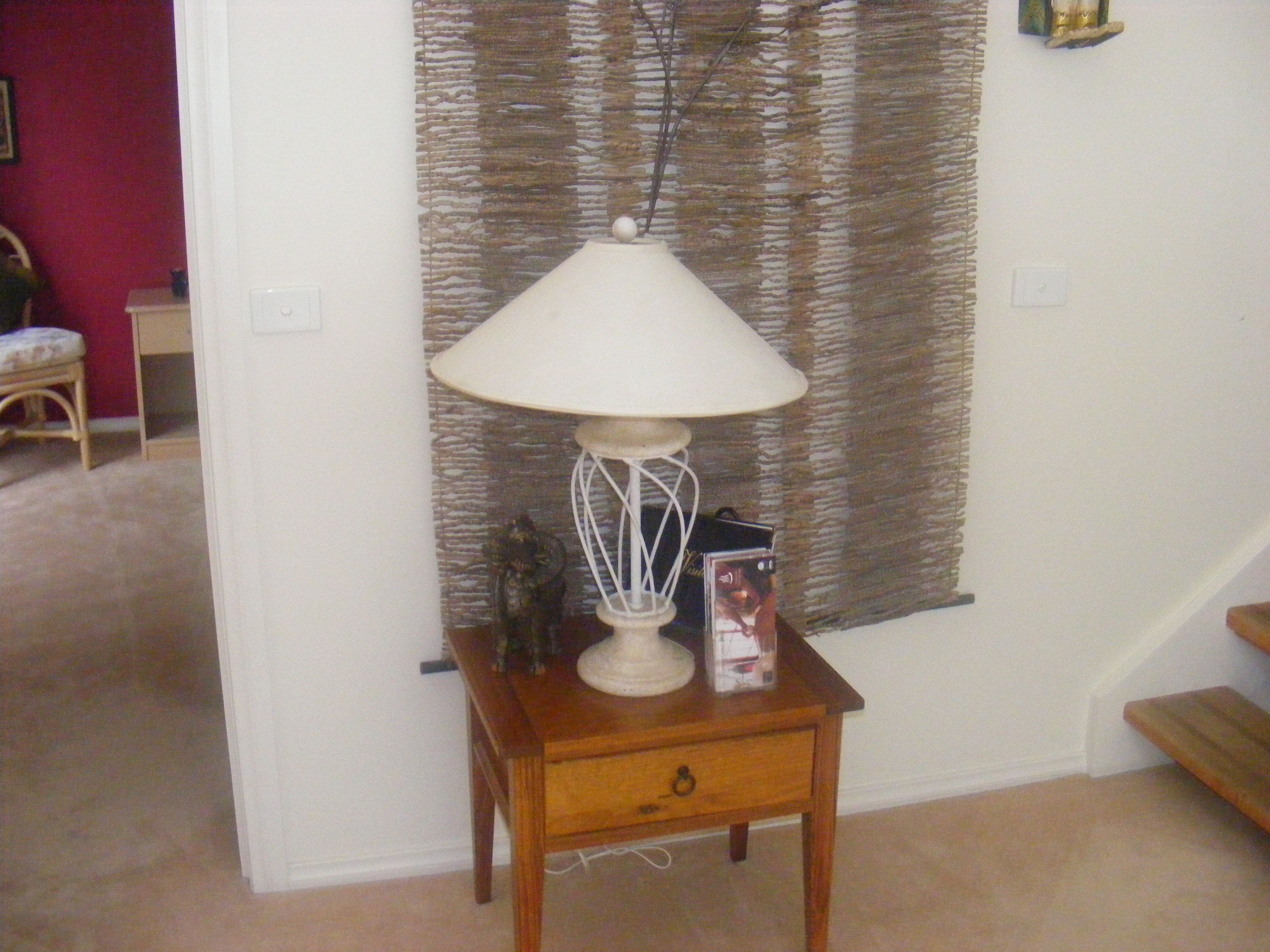 Una mesita de madera con una lámpara blanca, un pequeño adorno y una revista encima.