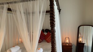 Een hemelbed met een baldakijn, een nachtkastje met een kaars, en een spiegel.