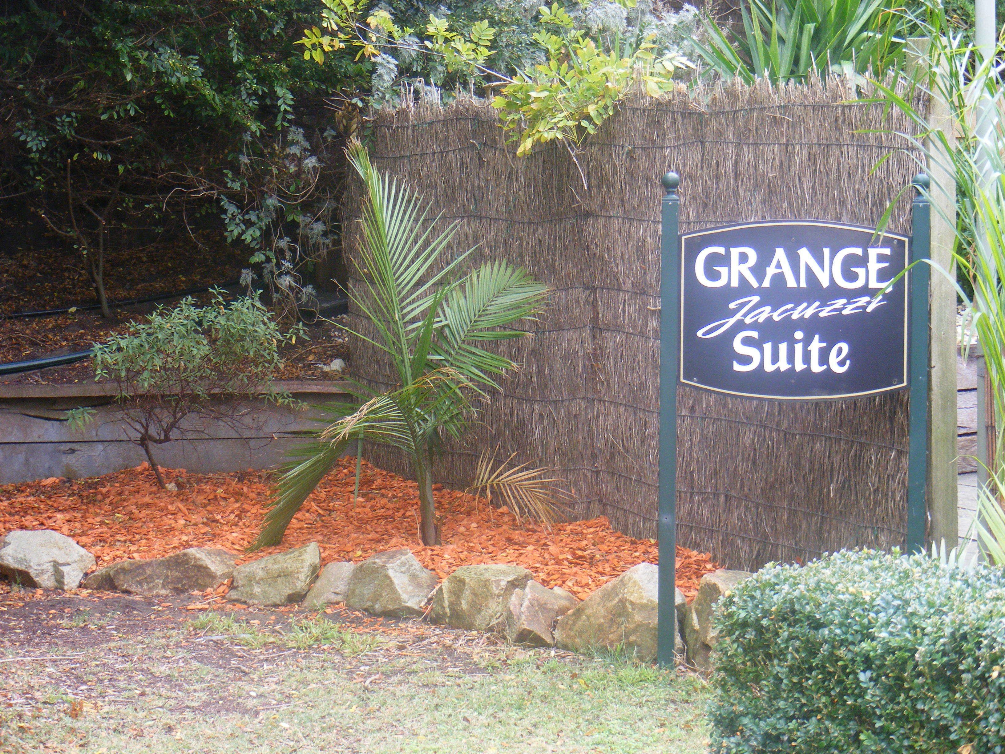 Une enseigne indiquant l’entrée de la « Grange Junction Suite », entourée d’un jardin aménagé avec des rochers, un palmier et divers arbustes.