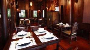 Comedor con mesas de madera dispuestas para cuatro comensales, cada una con mantel blanco y cubertería.