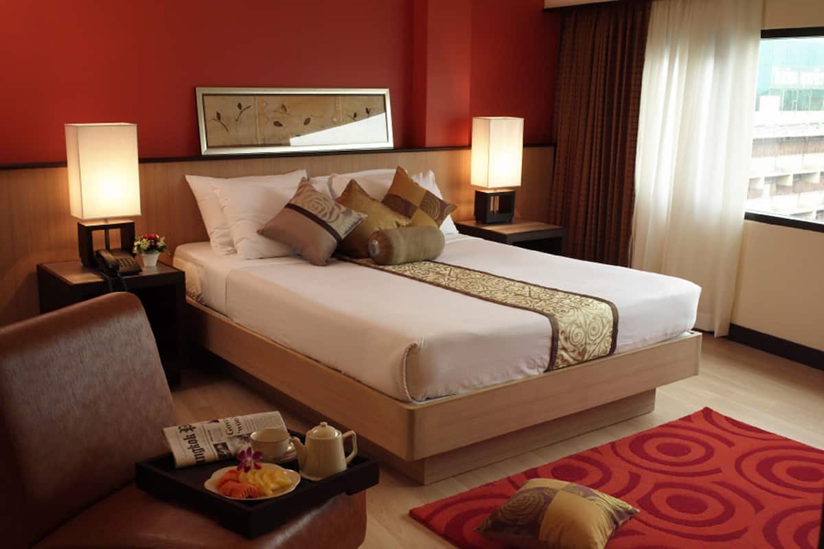 A hotel room with a large bed, two bedside tables with lamps, a chair, a tray with breakfast items, and a red patterned rug.